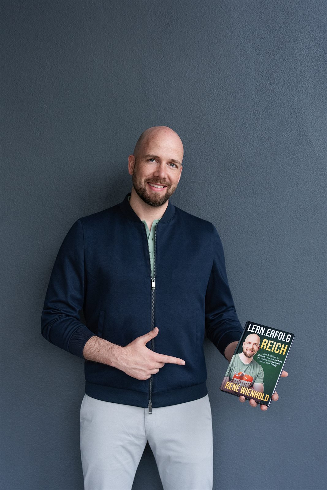 René Wienhold hält sein Buch Lern.Erfolg.Reich in der Hand und zeigt darauf